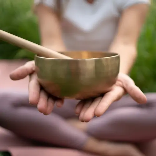 Monika Denca, sie hält eine Meditation Schale in den Händen, diese ist von sich gestreckt und der Fokus des Bildes. Der Rest ist unscharf.