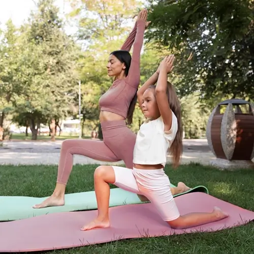 Mutter und ihr Kind beim Yoga. Beide stehen auf ihrer Matte in der Low Lunge mit Armhebung Asana. Anjaneyasana. Dabei schauen sie beide nach links.